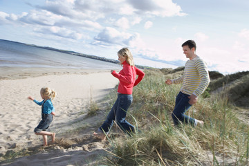 Parents and daughter (5-6) running onto beach