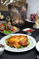 Baked full chicken with vegetables in a plate on a table next to glass of wine and candles. Outdoor, green park