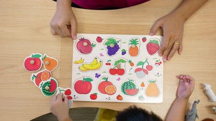 Cute little child girl having fun playing with montessori wood material for the fruits and vegetables learning at class room. Concept of educational toys for young children.