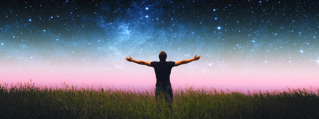 Man with arms wide open standing on the grass field against the night starry sky. Elements of this...