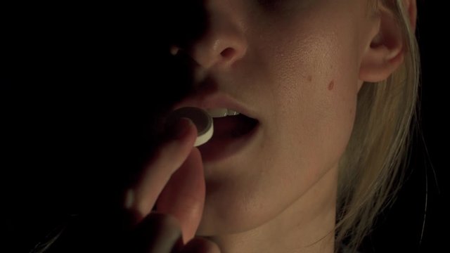 young woman taking pills. She puts a pill in her mouth and swallows it. Close-up.