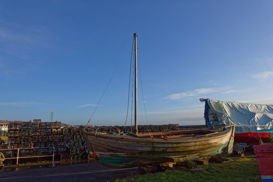An old wooden Fishing Boat with sail, parked up on the quayside next to the Pots and Creels in the Fishing Village of Johnshaven.