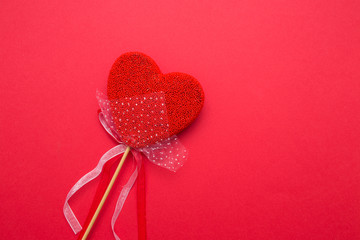 Closeup of a heart with a decor on a stick on a red isolated background.