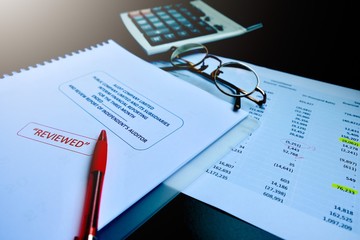 The reviewed financial statement, eyeglass, highlight pencil, calculator, laptop and edited paper. It's important work of the account, finance, internal and external audit must to accurate and timely