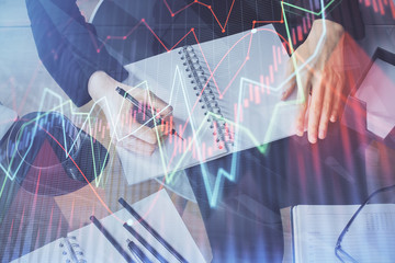 Forex chart hologram on hand taking notes background. Concept of analysis. Multi exposure