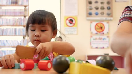 Cute little child girl having fun playing with cooking toys in living room at class room. Kid using wood toy knife slicing vegetables on chopping wood board. Concept of educational toys for young chil