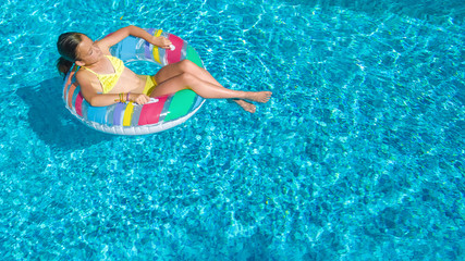 Acrive girl in swimming pool aerial top view from above, kid swims on inflatable ring donut , child has fun in blue water on family vacation resort