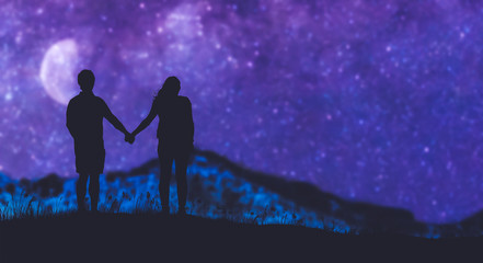 a silhouette boy and girl holding hands looking at the Milky Way in th mountains.