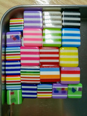 Multicolored striped rectangular beads lying in straight rows in a metal box
