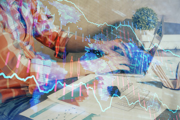 Double exposure of stock graph with businessman typing on computer in office on background. Concept of hard work.