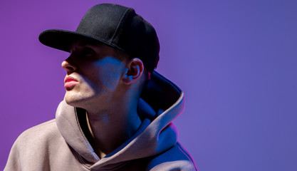 Men portrait in a neon light. Beneath in the hoodie and hat. Dark face. Hip-hop style.