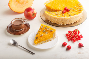 Traditional american sweet pumpkin pie decorated with hawthorn red berries and pumpkin seeds with cup of coffee on a white wooden background. side view.