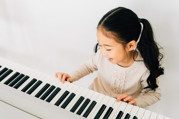 From above of happy smiling cute Asian girl playing piano enjoying time practicing music at home - 316711983