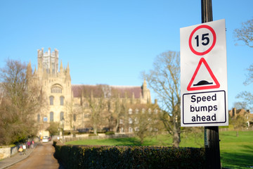 Shallow focus of a general speed limit and speed bump sign located nearby a large cathedral. Traffic calming measures are in place in the area.