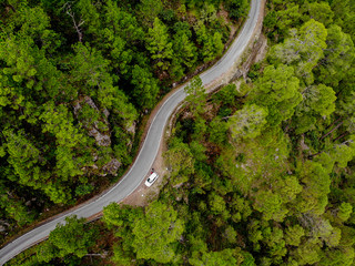 Aerial view of a vehicle on the road through a deep forest. Bird eye view of a Green Forest road. Drone shot.