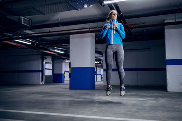 Fototapeta na wymiar Young fit attractive caucasian sportswoman in tracksuit running fast in garage. Urban life concept.
