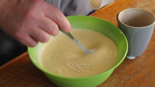 the man pours the semolina from the cup into the egg-curd mass and sews everything with a tablespoon into a single mass. close-up