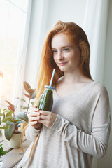 cheerful young smiling woman holding glass bottle of green healthy smoothie