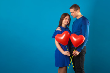 Fototapeta na wymiar young couple in love on a blue background with red balloons. Valentine's Day