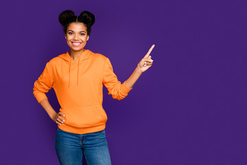 Photo of cheerful positive pretty cute girl pointing into empty space with hand on waist smiling...