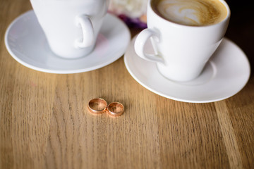 Close up of engagement rings, rose flower bouquet and coffee on table. 