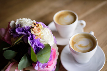 Close up of engagement rings, rose flower bouquet and coffee on table. 