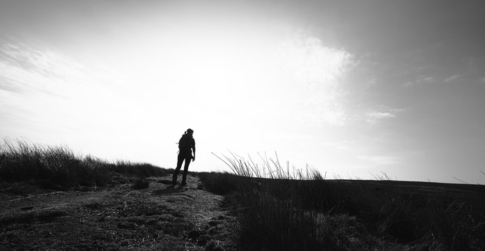 A black and white image of a an active female hiker walking along a countryside trail on a bright snny day.