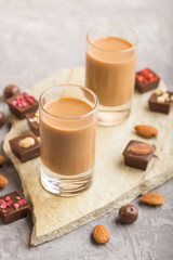 Sweet chocolate liqueur in glass on a gray concrete background and stone slate board. Side view, selective focus.