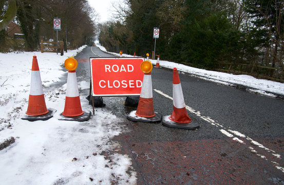 A red Road Ahead Closed sign due to adverse road conditions in winter, England, UK.