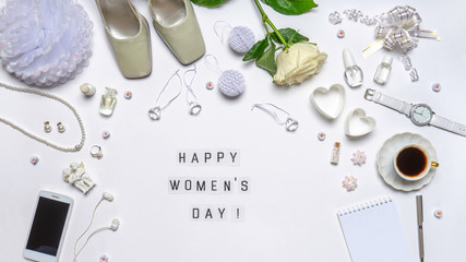 Text HAPPY WOMEN'S DAY. Stylish feminine accessories, decorative items, cosmetics, jewellery, hearts and rose flower on white background. Greeting card, flat lay, top view