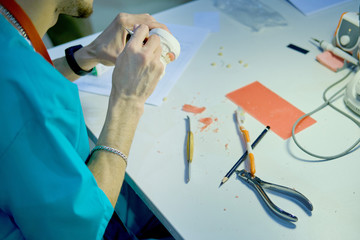 Dentures in the hands of a male dentist doctor. The prosthetist is working on the creation of a false jaw.