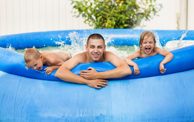 happy family, dad with son and daughter bathe in an inflatable pool, laugh cheerfully and make big splashes, vacation in the village