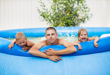 Fototapeta na wymiar happy family, dad with son and daughter bathe in an inflatable pool, laugh cheerfully and make big splashes, vacation in the village