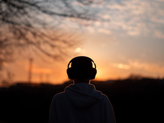 A young hipster man with headphones listens to music while walking in the Park and looks at the sunset