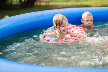 happy cute children, preschoolers, fair-haired blue-eyed brother and sister bathe in the summer in the village in the inflatable pool, make splashes and laugh joyfully