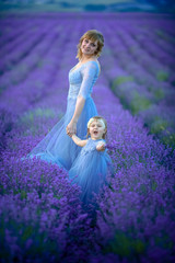 Mother dressed in a wedding dress with her daughter are on the agricultural lavender field.