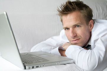 Man in smart casual unbuttoned white shirt lying on white sofa with his laptop computer 