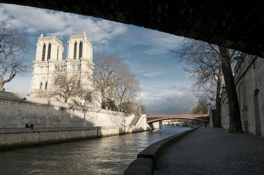 Bright winter view of Notre Dame Cathedral from the shadowy recesses of a quay on the River Seine