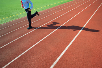 Unrecognizable businessman running along empty track with his shadow