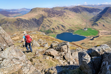 A hiker descending the summit of High Stile towards Lake Buttermere on a sunny spring day in the English Lake District.