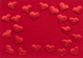 Small textile red hearts are on a background of red velvet paper.