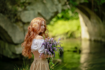 Naklejka premium A woman in a long dress walks near the forest old bridge over the river.