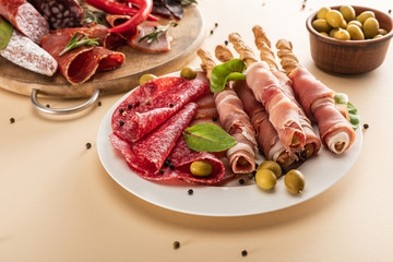 delicious meat platters served with olives, spices and breadsticks on plate and wooden board on beige background