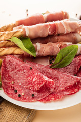 delicious meat platter served with olives, spices and breadsticks on plate on beige background