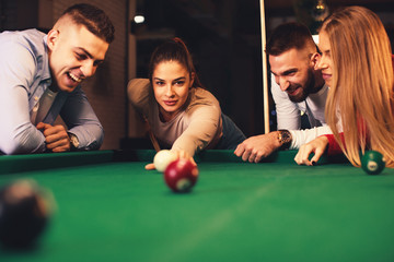 Group of friends play billiards at night out