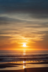 Fototapeta premium Vertical image of a sunrise along the Atlantic Coast of Port Orange, Florida, featuring a silhouetted man on a bicycle riding on a the beach. 
