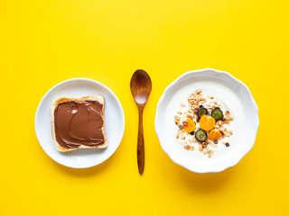 Müsli mit Joghurt und frischen Früchten und Toastbrot mit Schokocreme auf einem gelben Hintergrund, Gegensätze