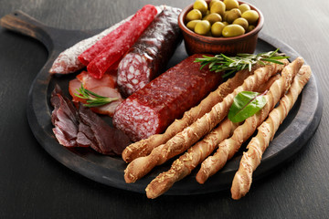 tasty meat platter served with olives and grissini on board on black surface
