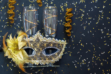 golden venetian mask with champagne glasses and confetti on black background
