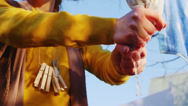 housewife in yellow wrings towel on rope in yard closeup